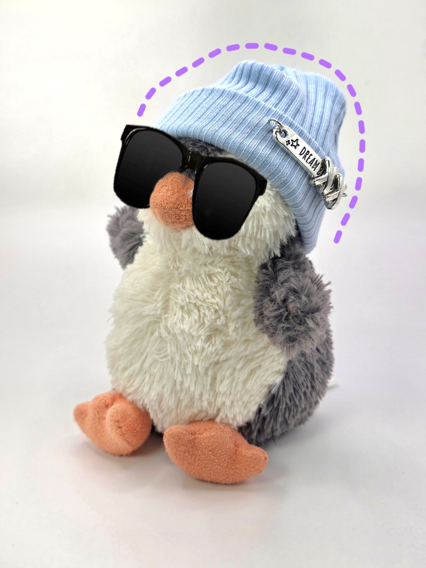 Stuffed penguin toy wearing sunglasses and a blue beanie with a tag on a white background