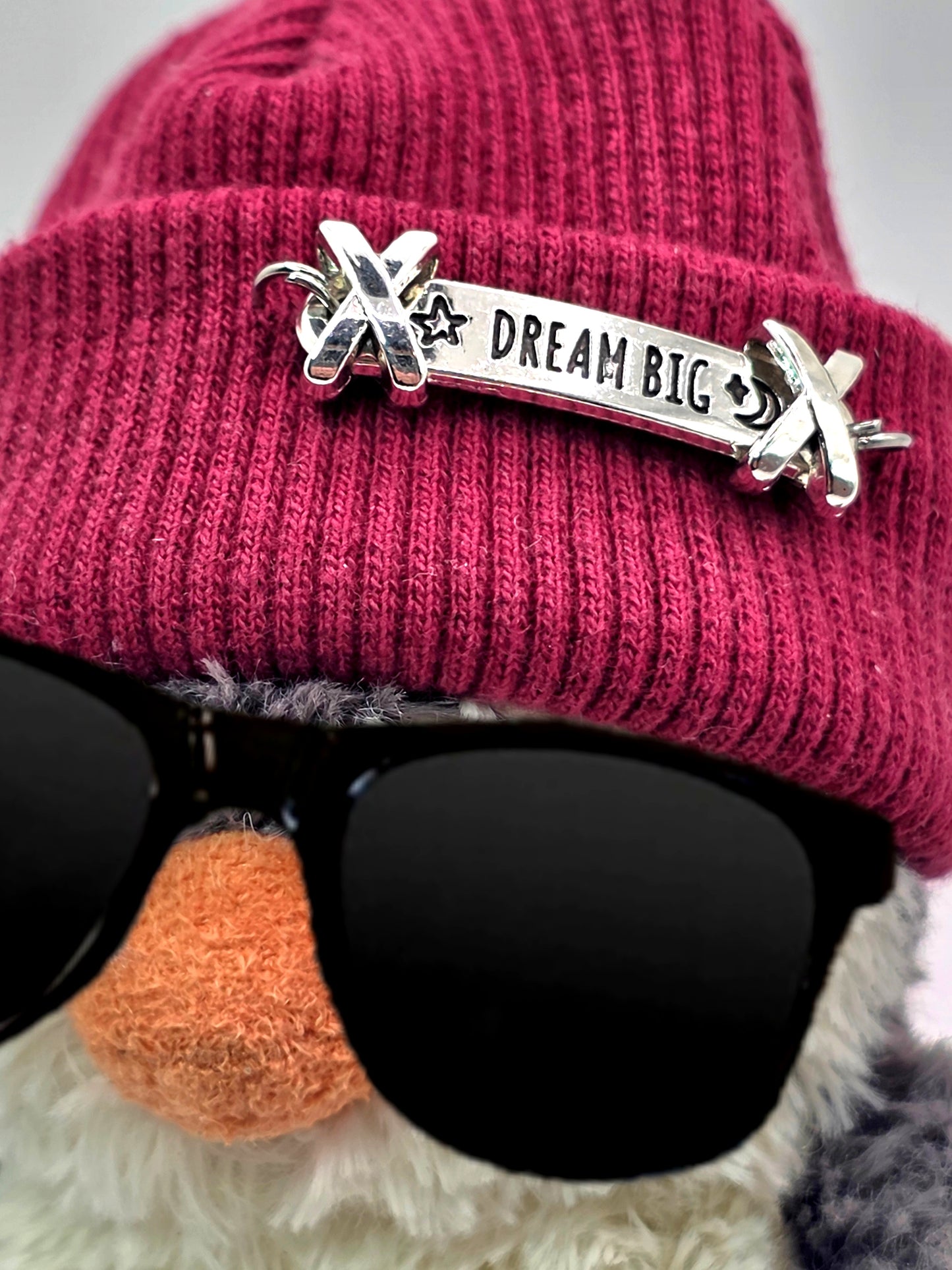 Pink beanie with 'Dream Big' pin and sunglasses on a white background