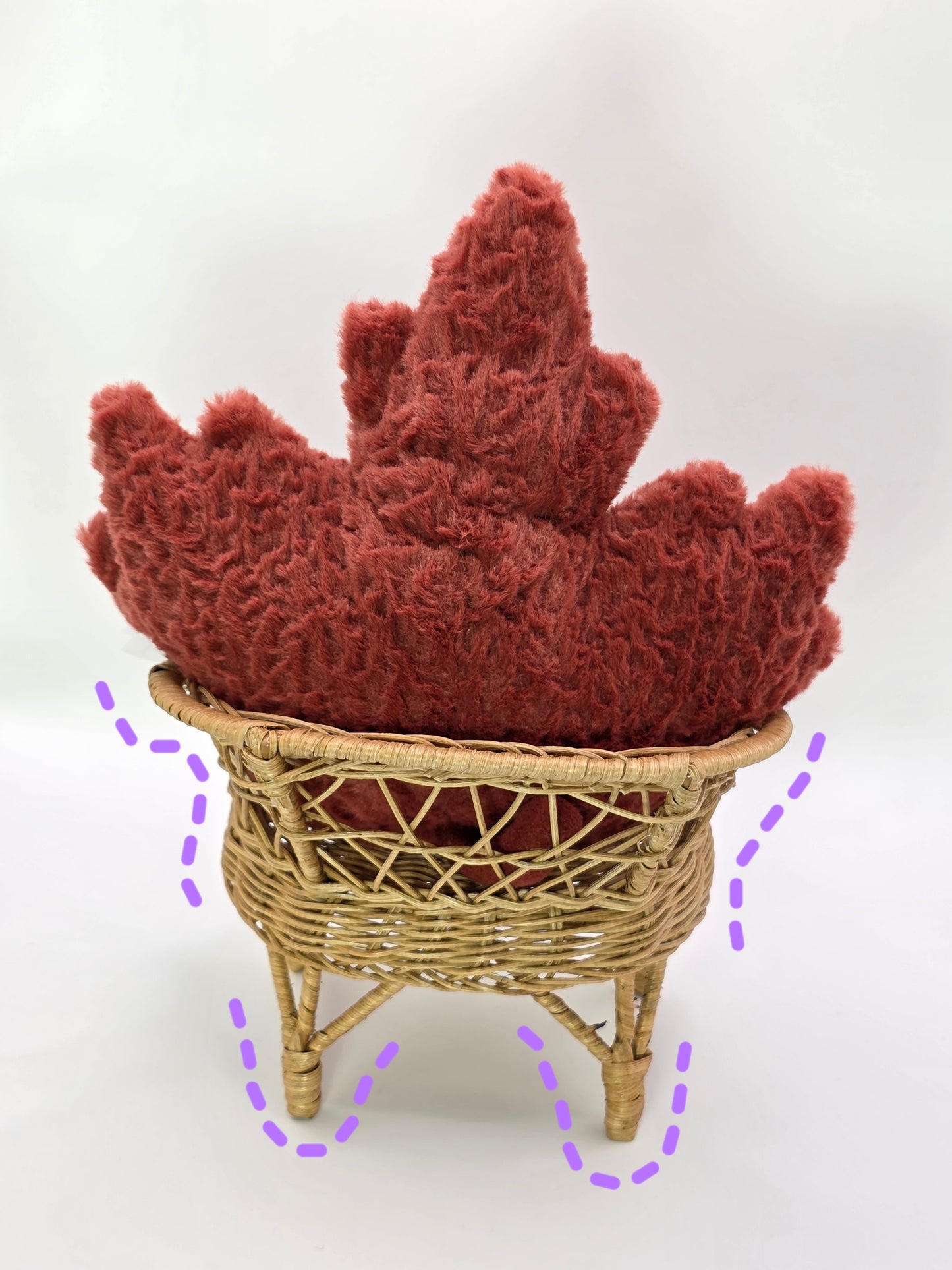 Red maple leaf-shaped stuffed animal on a wicker stool against a white background