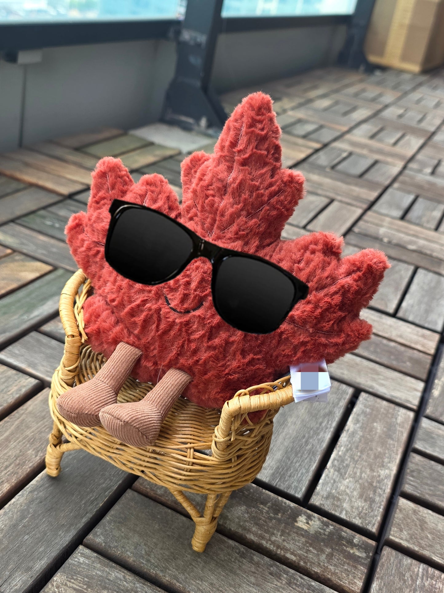 Red maple leaf toy with sunglasses sitting in a small handmade chair on a wooden deck.