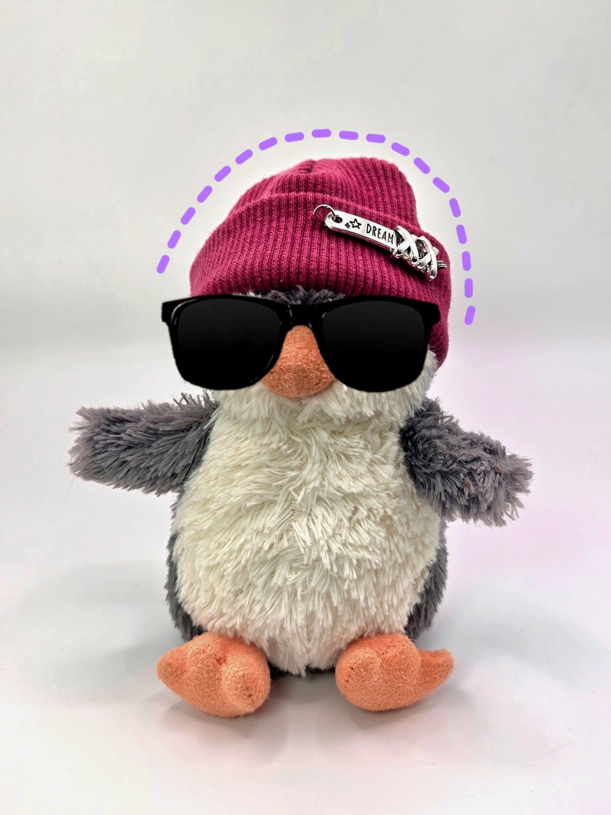 Plush penguin wearing sunglasses and a pink beanie with a small flag on a white background