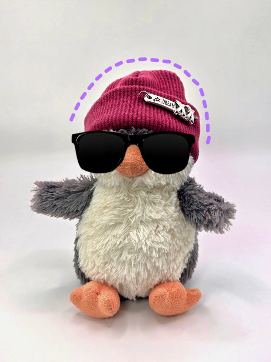 Plush penguin wearing sunglasses and a pink beanie with a small flag on a white background